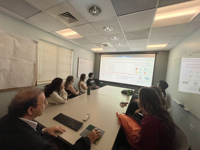 Students sit around a table watching a presentation